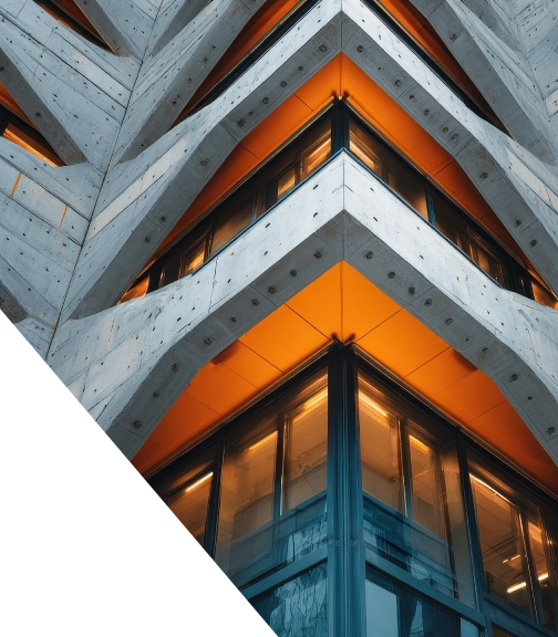 Low-angle view of a modern brutalist building corner, featuring raw concrete geometric beams contrasting with warm orange underlit ceilings and glass windows.
