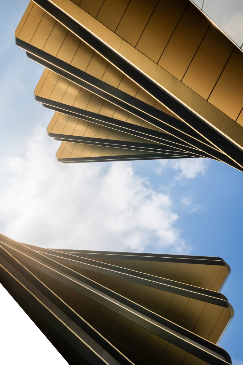 Low-angle view of futuristic gold architectural structures fanning out against a blue sky with soft white clouds.