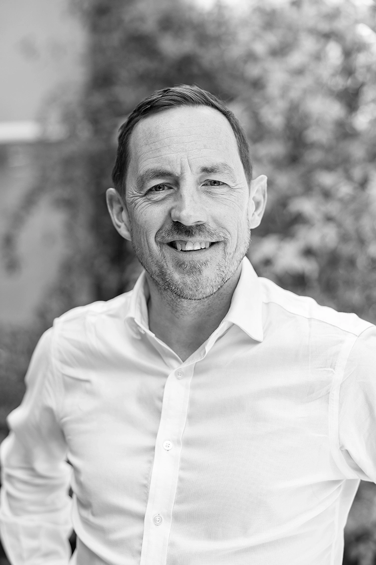 Black and white headshot of a smiling man in a white button-down shirt.